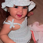 Dalia joined the competition — help win amazing prizes! baby, child, smiling, hat, dress, couch, blanket, indoor, cute, happy, face, person, infant, sitting, skin, tongue, comfortable, cozy, soft_lighting, playful