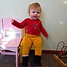 bead_maze, black_boots, carpet, chair, child, floor, happy, indoor, pink_chair, playroom, red_shirt, smiling, toddler, toy, train_track, wall, waving, wooden_toy, yellow_chair, yellow_pants