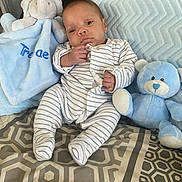 Trenae is registered to the contest to win money with this photo: baby, infant, striped_onesie, plush_elephant, blue_teddy_bear, blanket, pillow, patterned_bedspread, indoor, child, cute, soft_toys, seated, portrait, newborn, cozy, comfort, resting, small_hands, striped_clothing