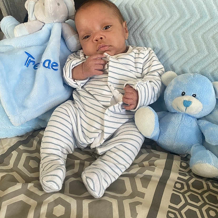 Trenae is registered to the contest to win money with this photo: baby, blanket, blue_teddy_bear, child, comfort, cozy, cute, indoor, infant, newborn, patterned_bedspread, pillow, plush_elephant, portrait, resting, seated, small_hands, soft_toys, striped_clothing, striped_onesie