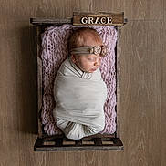 Grace joined the competition — help win amazing prizes! newborn, baby, swaddled, crate, wooden_floor, pink_blanket, headband, sleeping, indoors, infant, wrapped, cute, soft_texture, peaceful, portrait, resting, wood, decor, baby_girl, cozy