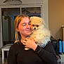 Vaïanna participe au concours pour gagner de l'argent avec cette photo : woman, dog, pomeranian, fluffy_dog, indoor, smiling, holding, black_top, animal, pet, affection, table, chair, living_room, window, lamp, suitcase, furniture, casual, portrait