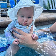Rosalia joined the competition — help win amazing prizes! adult_hand, baby, blue, chair, child, cute, daylight, fence, hand, outdoor, person, pool, relaxation, sitting, sky, summer, sunhat, swimsuit, water, water_reflection