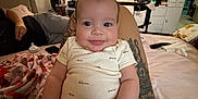 Rosalia is registered to the contest to win money with this photo: adult, baby, bedroom, blanket, bottle, clothing, decor, door, furniture, happy, infant, interior, lamp, person, remote_control, shelf, sitting, smiling, tattoo, toy
