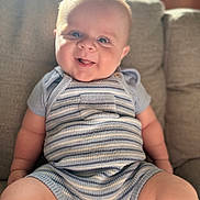 Alfie is registered to the contest to win money with this photo: baby, infant, smiling, cute, striped_clothing, romper, knitwear, seated, couch, indoor, soft_light, cheeks, tongue_out, happy, child, person, portrait, plush, cozy, comfortable
