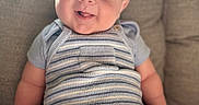 Alfie is registered to the contest to win money with this photo: baby, infant, smiling, cute, striped_clothing, romper, knitwear, seated, couch, indoor, soft_light, cheeks, tongue_out, happy, child, person, portrait, plush, cozy, comfortable