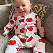 Alfie is registered to the contest to win money with this photo: baby, child, smiling, onesie, red_tomato_pattern, couch, cushion, indoor, fan, happy, portrait, infant, clothing, fabric, head, face, person, seated, comfort, home