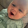 Alfie is registered to the contest to win money with this photo: baby, child, face, smile, happy, knitted_sweater, green_clothing, couch, texture, close_up, infant, skin, eyelashes, mouth_open, head, person, indoors, portrait, young_child, cozy