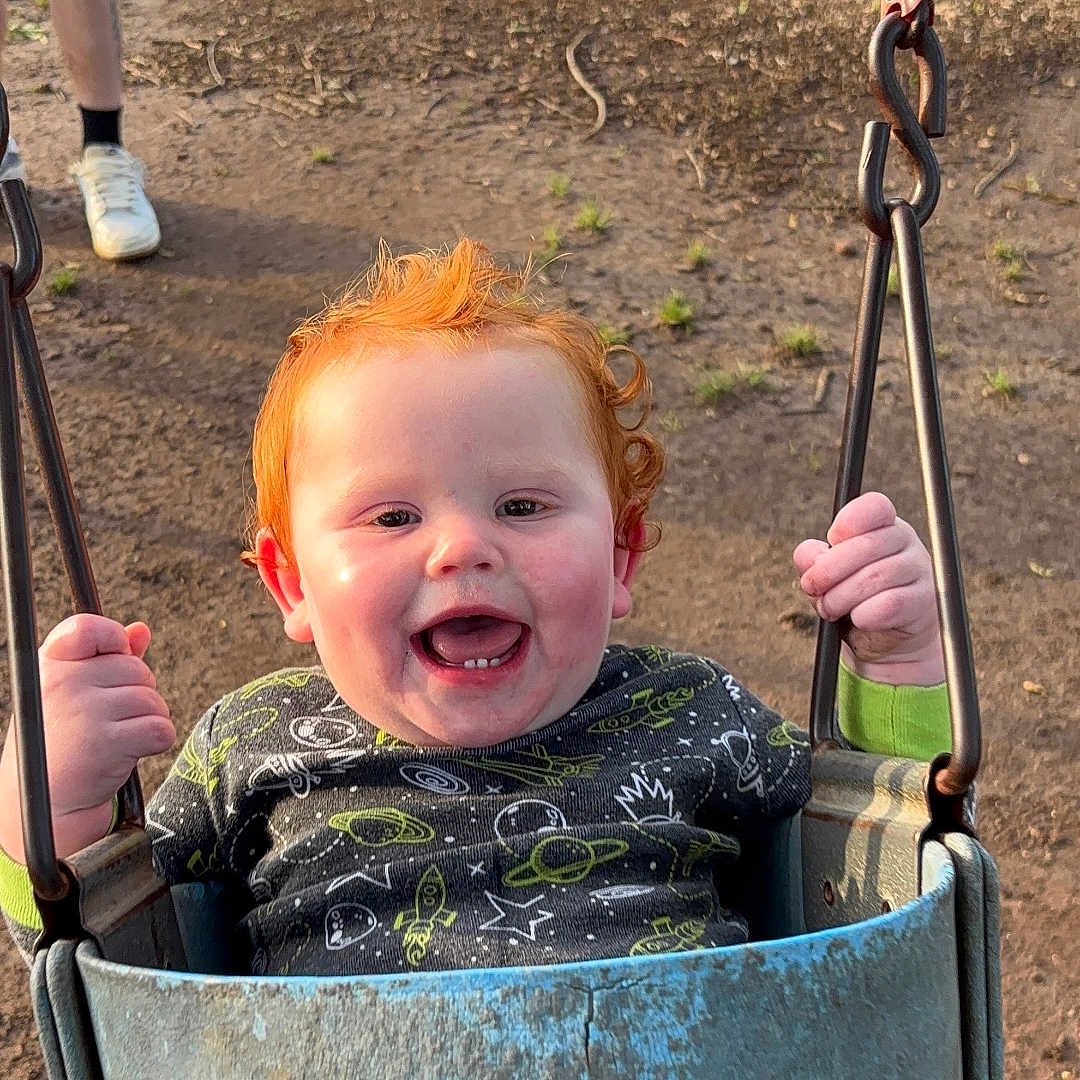 Malakai Dean joined the competition — help win amazing prizes! camouflage_pants, casual_wear, chain, child, clothing, daylight, dirt, grass, hand, happy, legs, nature, outdoor, person, playground, red_hair, seat, smiling, swing, toddler