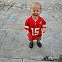 Jordan is registered to the contest to win money with this photo: toddler, child, smiling, red_jersey, football_jersey, shorts, black_shoes, outdoor, concrete, playful, happy, toy, standing, casual_clothing, young_child, daylight, cute, expression, person, fun