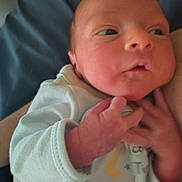 Dakota is registered to the contest to win money with this photo: baby, newborn, infant, face, eyes, hand, onesie, clothing, blanket, bedding, portrait, close_up, cheek, skin, nose, mouth, chubby_cheeks, palm, pajamas, holding