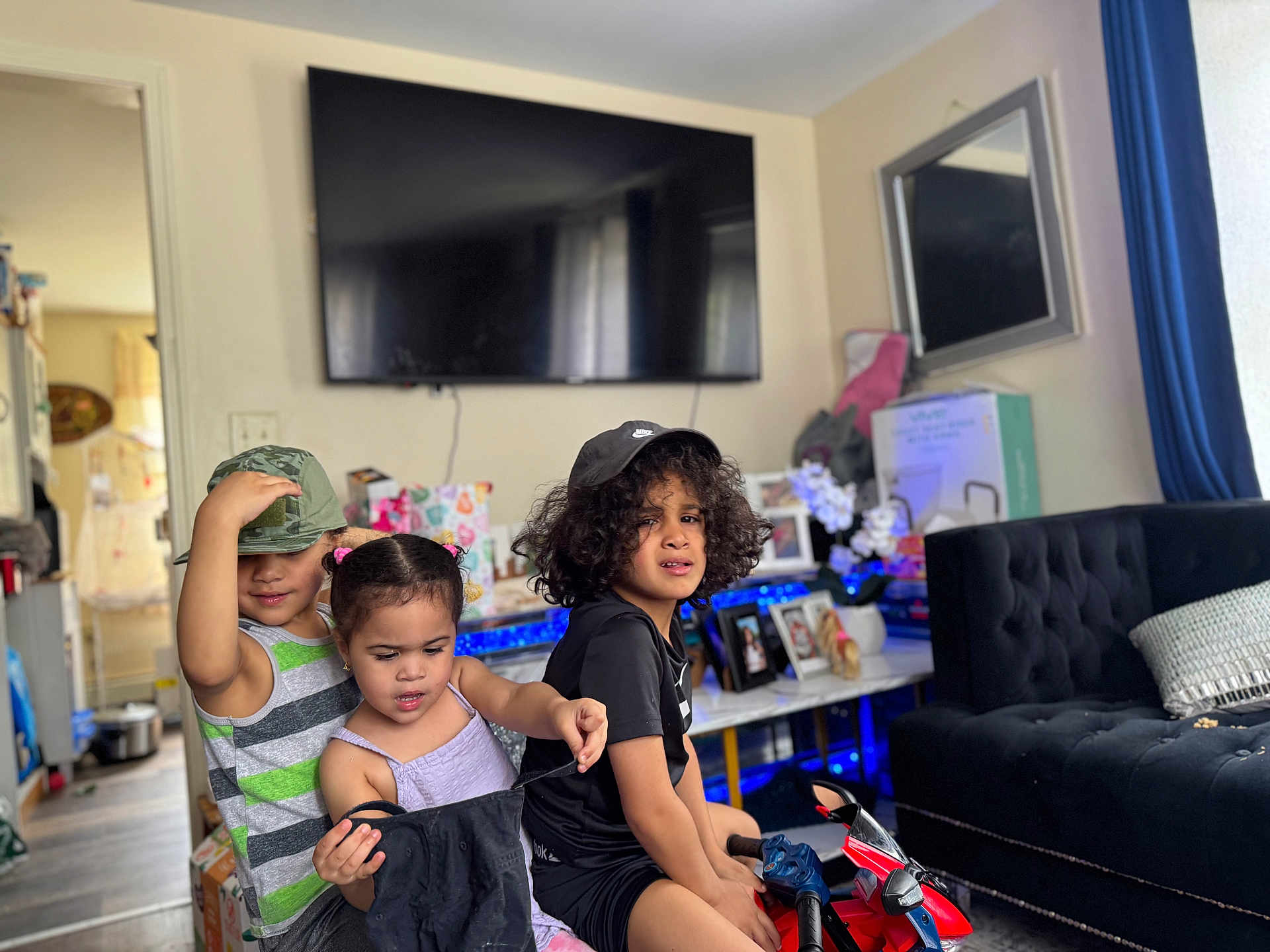 Rose joined the competition — help win amazing prizes! children, indoor, play, toy_motorcycle, cap, curly_hair, black_tshirt, striped_shirt, pigtails, living_room, television, couch, photos, table, curtains, floor, playful, kids, furniture, home