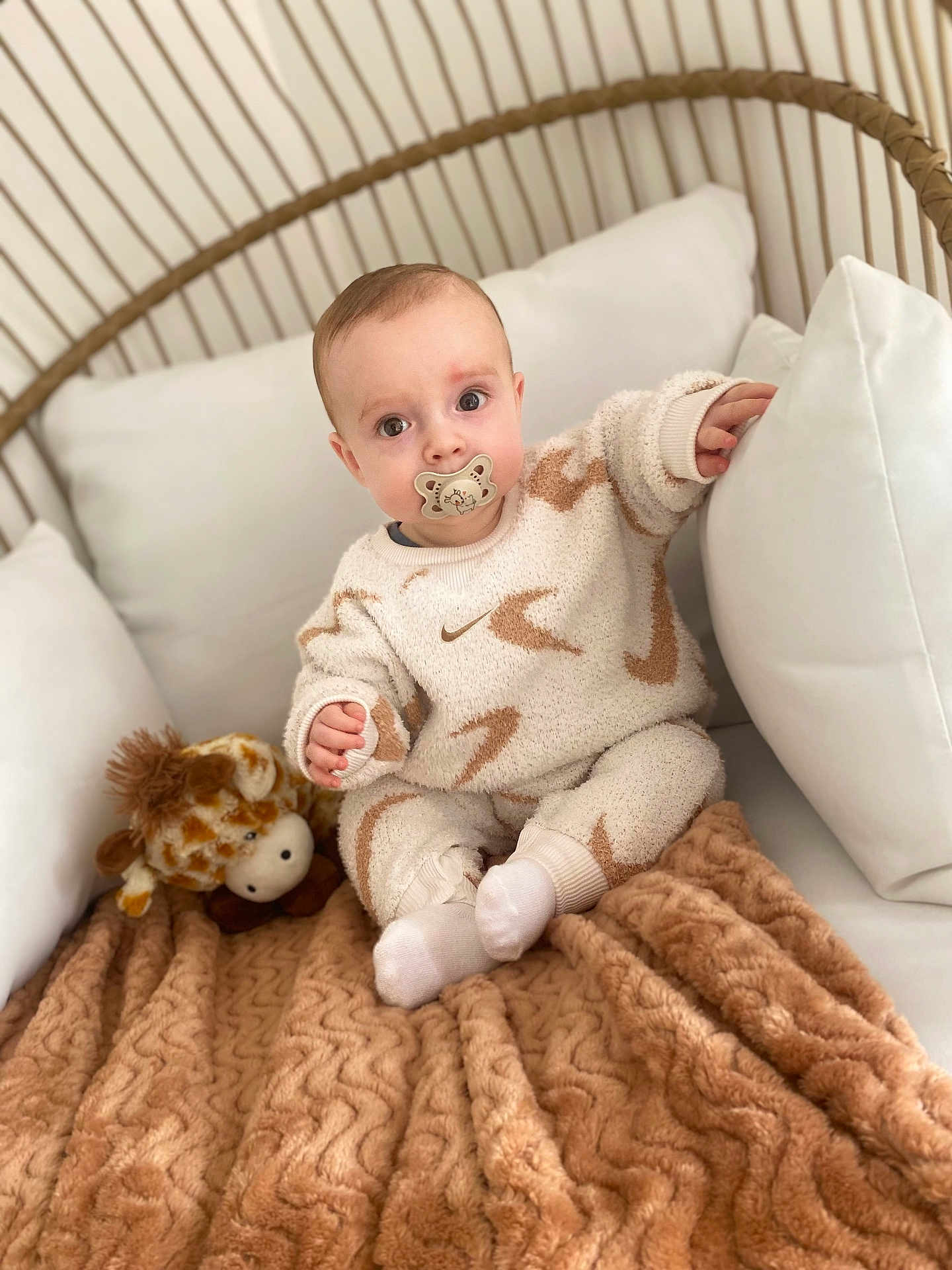 Liam participe au concours pour gagner de l'argent avec cette photo : baby, pacifier, blanket, plush_toy, giraffe, chair, wicker, cozy, child, clothing, socks, cute, infant, indoor, soft_texture, pattern, person, seated, comfortable, portrait