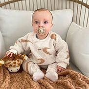 Liam a rejoint le concours — aidez-le/la à gagner de superbes lots ! baby, pacifier, plush_toy, giraffe, blanket, pajamas, indoor, couch, cushions, child, cute, infant, soft_toys, sitting, portrait, cozy, furniture, neutral_expression, young_child, home