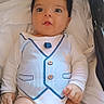 baby, child, infant, portrait, lying_down, stroller, white_clothing, striped_vest, onesie, wide_eyes, facial_expression, dark_hair, light_skin, indoor, soft_lighting, blanket, cushion, buttons, fashion, close_up
