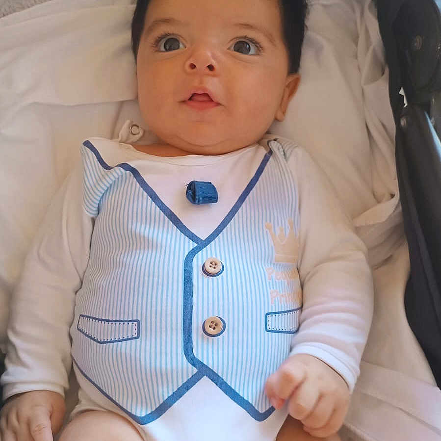 Emir Ismael joined the competition — help win amazing prizes! baby, child, infant, portrait, lying_down, stroller, white_clothing, striped_vest, onesie, wide_eyes, facial_expression, dark_hair, light_skin, indoor, soft_lighting, blanket, cushion, buttons, fashion, close_up