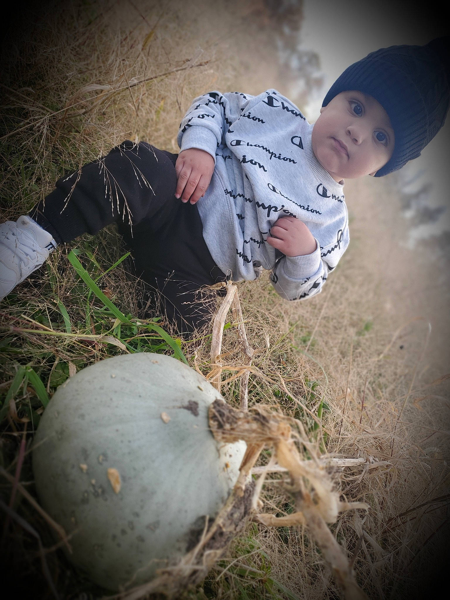 Anthem is registered to the contest to win money with this photo: baby, ball, boot, cap, flash_photography, grass, grass_family, happy, hat, head, headwear, human_leg, landscape, people_in_nature, person, plant, sitting, sneakers, soil, sun_hat
