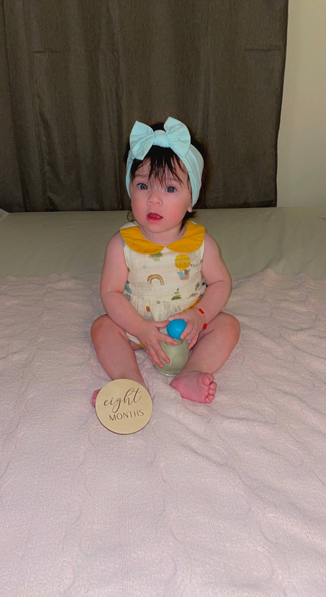 Bloom is registered to the contest to win money with this photo: baby, baby_toddler_clothing, cheek, comfort, face, finger, flooring, foot, fun, head, headgear, human_leg, linens, person, pink, room, sitting, skin, sleeve, surprise