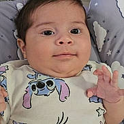 Lucas is registered to the contest to win money with this photo: baby, infant, face, eyes, hand, pillow, clothing, cartoon_print, smile, skin, hair, lying_down, indoors, child, cute, expression, young, app_interface, phone_screen, star_pattern