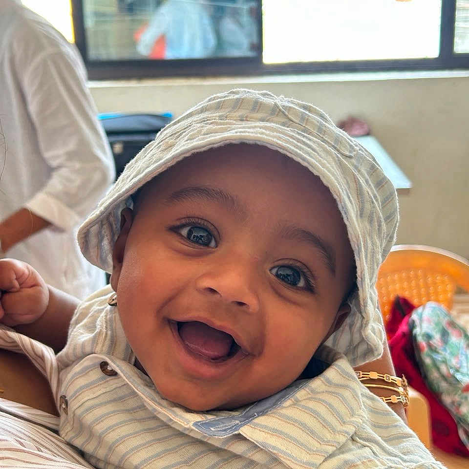Cornelius Ivan is registered to the contest to win money with this photo: baby, bright_eyes, casual_clothing, child, closeup, cute, face, happy, hat, headwear, holding, indoor, infant, joyful, person, portrait, seated, smiling, striped_clothing, young_child