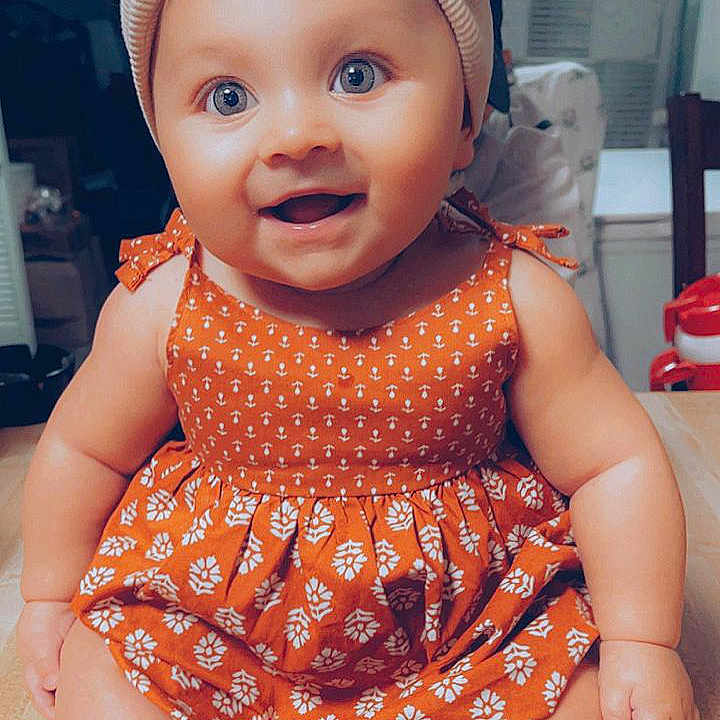 Izzabelle is registered to the contest to win money with this photo: advertisement, baby, bonnet, cap, clothing, couch, dress, face, furniture, happy, hat, head, pattern, person, photography, portrait, poster, sitting, smile, toy