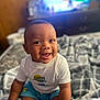 baby, bed, blanket, blue_shorts, child, clothing, cozy, cute, face, happy, home, indoor, infant, person, portrait, sitting, smiling, soft_light, warm, white_shirt