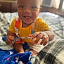 baby, bed, blanket, child, clothing, colorful, cozy, cute, expressive, face, happy, indoor, infant, person, playful, portrait, reaching_hand, sitting, smiling, young_child