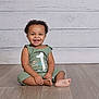 baby, birthday, celebration, child, clothing, curly_hair, cute, floor, green_outfit, happy, indoors, infant, one_year_old, person, portrait, sitting, smiling, toes, white_background, wooden_floor