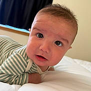 Damian is registered to the contest to win money with this photo: baby, infant, face, eyes, mouth, striped_clothing, bed, white_bed, soft, curious, indoors, portrait, closeup, head, skin, person, young_child, sleepwear, blanket, window