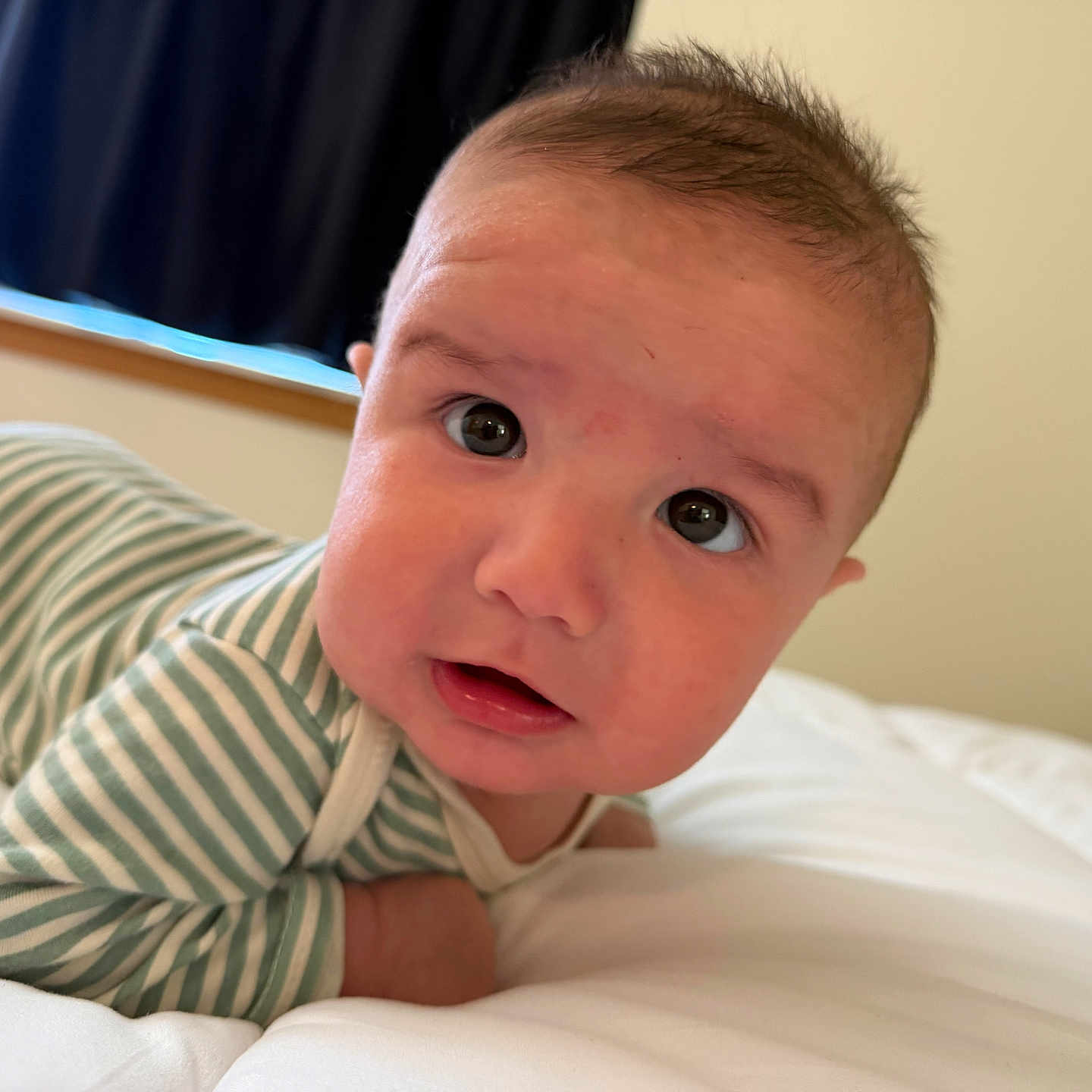 Damian is registered to the contest to win money with this photo: baby, bed, blanket, closeup, curious, eyes, face, head, indoors, infant, mouth, person, portrait, skin, sleepwear, soft, striped_clothing, white_bed, window, young_child