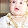 Abby is registered to the contest to win money with this photo: baby, child, closeup, curious, cute, decorative, expression, face, fashion, gold_embroidery, head, headpiece, indoors, infant, person, portrait, small, soft_lighting, white_clothing, young