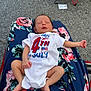 Rynleigh is registered to the contest to win money with this photo: newborn, baby, infant, sleeping, onesie, clothing, floral_blanket, fabric, legs, feet, hand, pavement, outdoor, red_chair, celebration, holiday, american_flag, text, person, resting