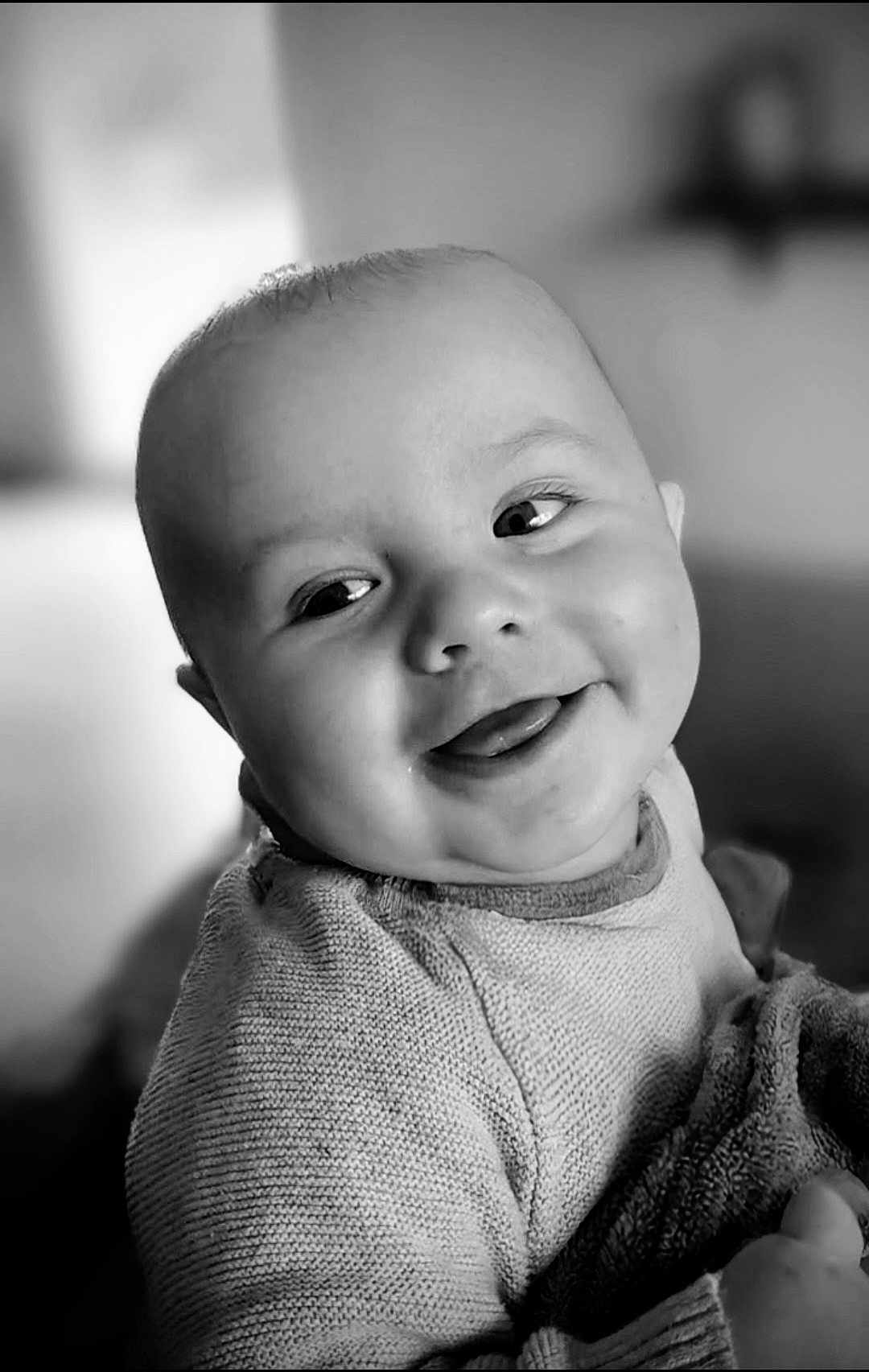 Andréas participe au concours pour gagner de l'argent avec cette photo : baby, smiling, tongue_out, sweater, blanket, face, portrait, close_up, child, cute, infant, happy, soft_light, indoor, cozy, expression, person, young_child, black_and_white, warm