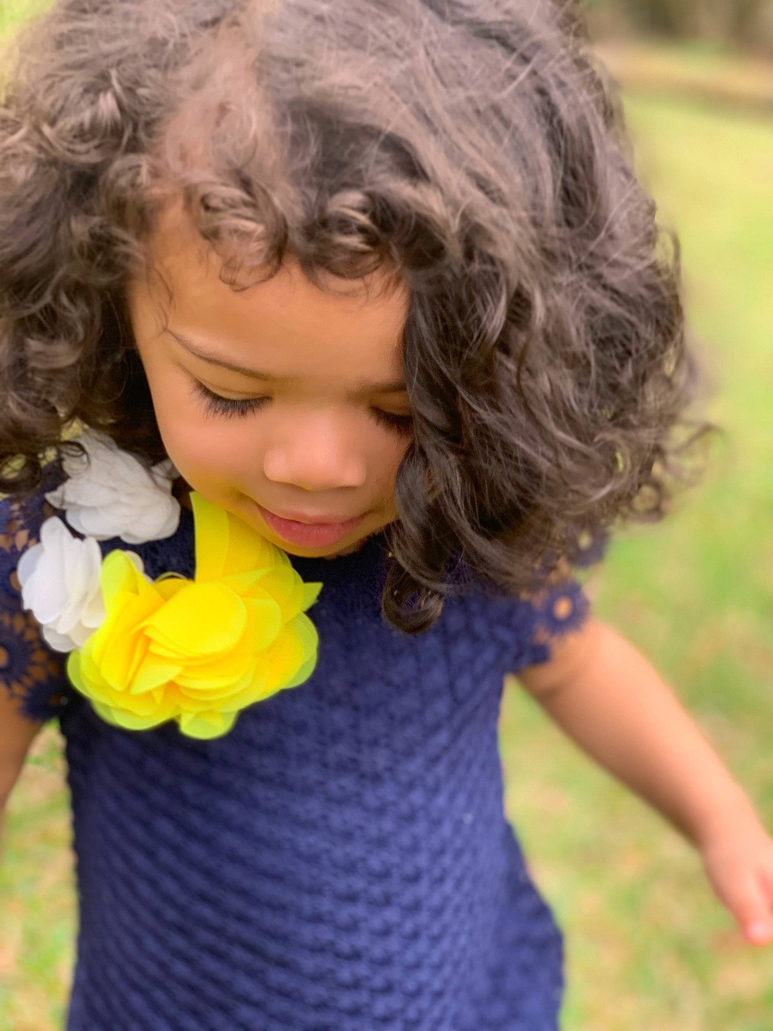 Bella is registered to the contest to win money with this photo: black_hair, brown_hair, child, child_model, flower, grass, hair, hairstyle, long_hair, neck, nose, people_in_nature, person, plant, play, skin, smile, toddler, yellow