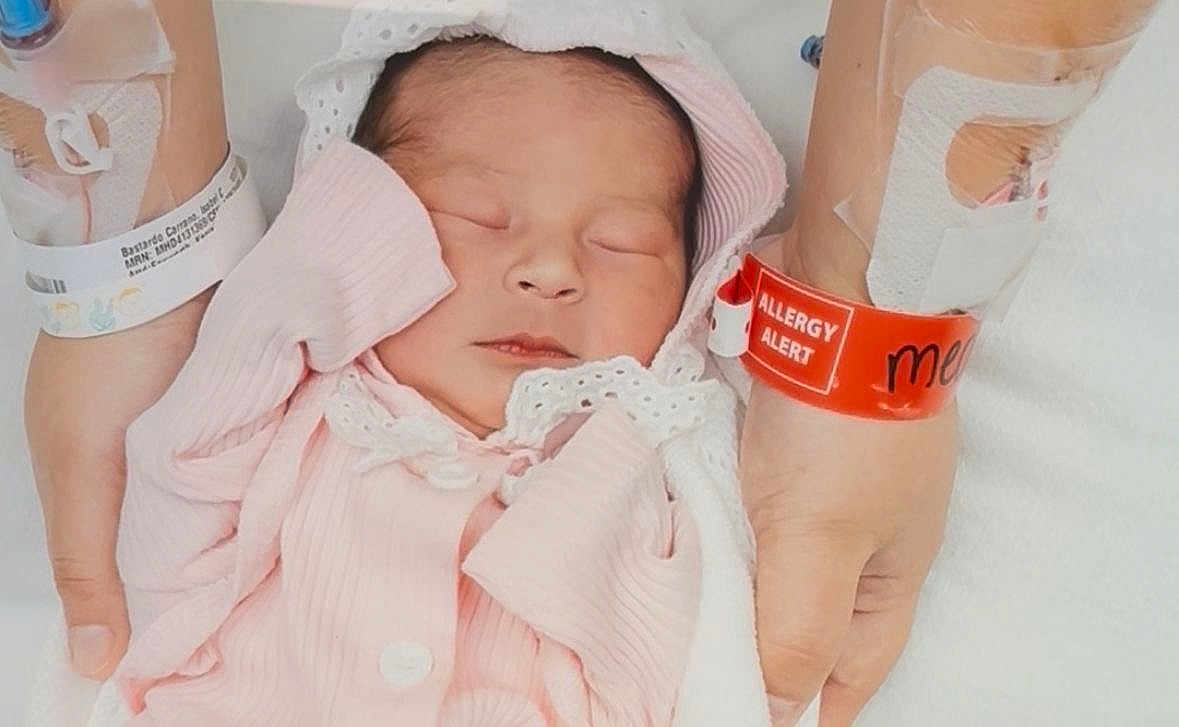 Isabella joined the competition — help win amazing prizes! newborn, baby, infant, sleeping, pink_clothing, wrapped, hands, hospital, medical_wristband, allergy_alert, adult_hands, patient, bed, blanket, soft_texture, closeup, portrait, healthcare, resting, peaceful