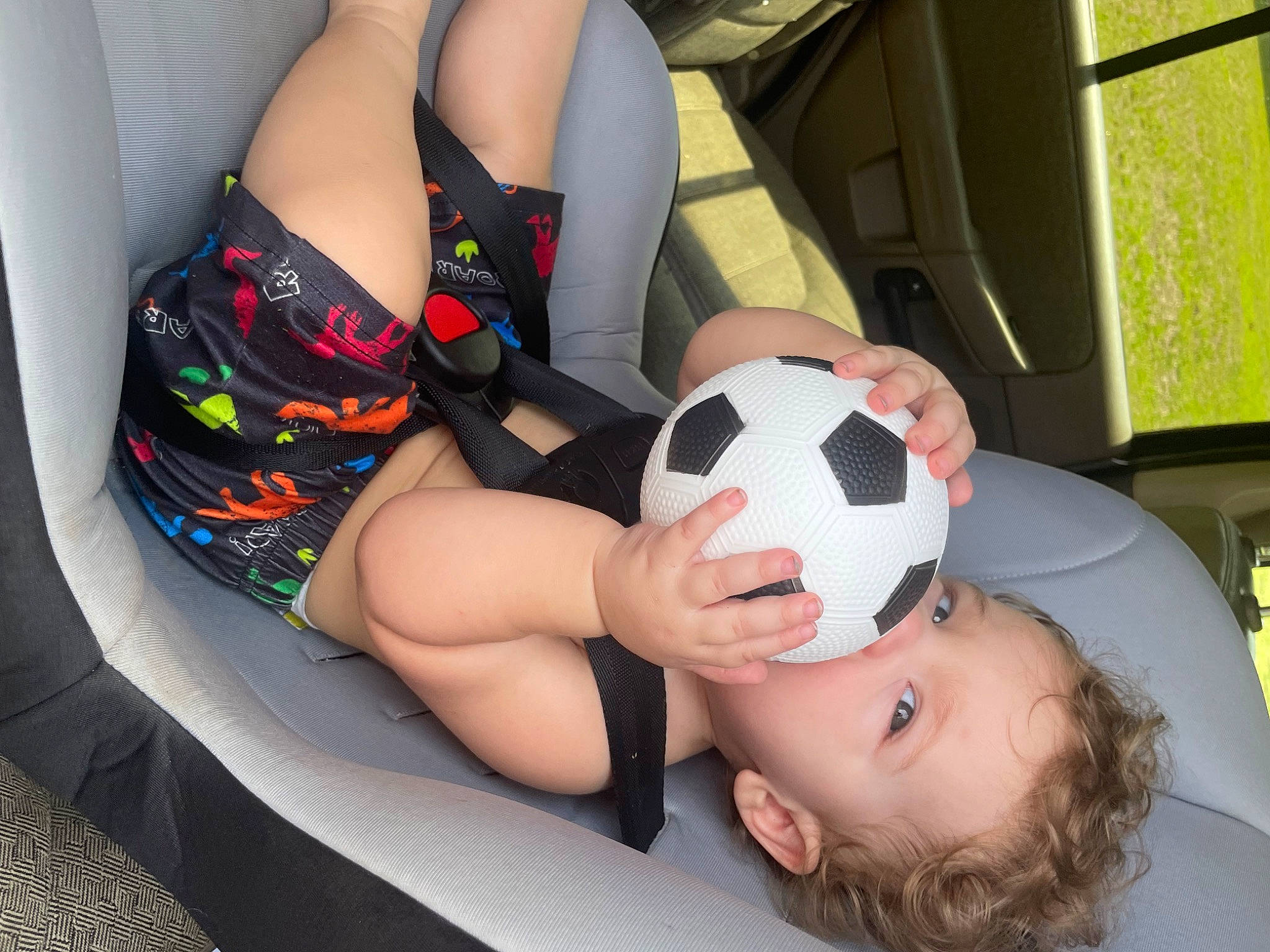 Cillian is registered to the contest to win money with this photo: automotive_design, ball, black_hair, carmine, child, comfort, facial_expression, foot, football, fun, happy, human_leg, knee, lap, leg, leisure, person, personal_protective_equipment, sitting, soccer