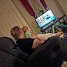 adult, baby, blanket, candid, colorful, cozy, cuddling, family, home, indoor, infant, living_room, parent, playmat, portrait, relaxed, seated, sofa, television, toys