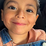 Aria is registered to the contest to win money with this photo: child, face, smile, portrait, denim_overalls, clothing, person, happy, young, casual_wear, car_seat, seat, closeup, eyelashes, skin, button, fabric, head, cute, indoors