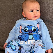 Liyah participe au concours pour gagner de l'argent avec cette photo : baby, child, pajamas, blue_clothing, stitch_character, face, eyes, ear, hand, foot, couch, fabric, pacifier, sitting, indoor, cute, comfort, soft, expression, person