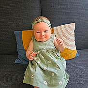 Cassie participe au concours pour gagner de l'argent avec cette photo : baby, child, dress, headband, couch, pillow, smile, sitting, indoors, cute, green, floral_pattern, happy, portrait, infant, clothing, face, person, home, comfort