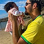 baby, man, beach, sky, clouds, sand, water, holding, smiling, yellow_shirt, pink_dress, happy, portrait, outdoor, family, love, glasses, short_hair, casual, sunny