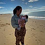 Anaïa a rejoint le concours — aidez-le/la à gagner de superbes lots ! woman, baby, beach, sand, ocean, sunlight, clouds, denim_jacket, leopard_print_pants, white_sneakers, holding_baby, outdoor, footprints, sky, nature, portrait, mother_and_child, love, peaceful, daytime