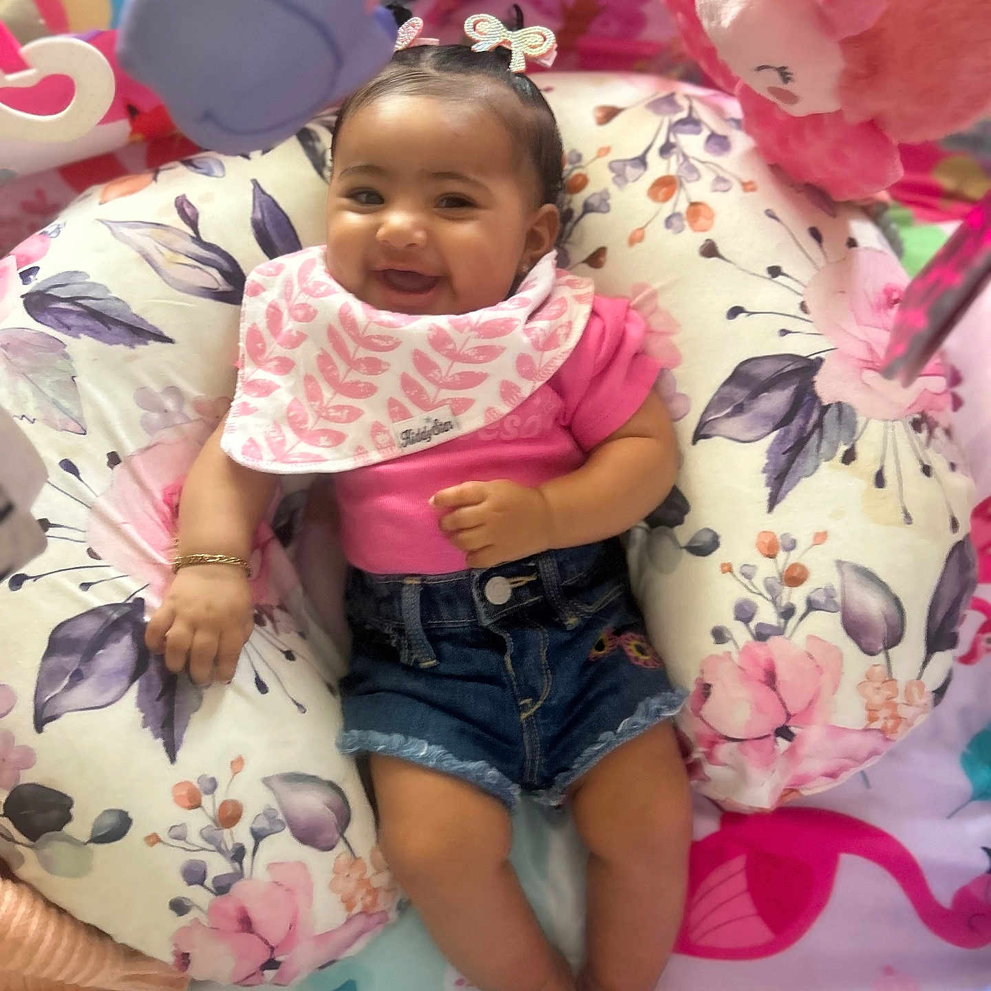 Zeari is registered to the contest to win money with this photo: baby, baby_clothing, bow_hair, bracelet, child, colorful, cushion, cute, denim_shorts, floral_pattern, happy, indoors, infant, lying_down, pink_shirt, playmat, plush_toys, portrait, smiling, soft_toys