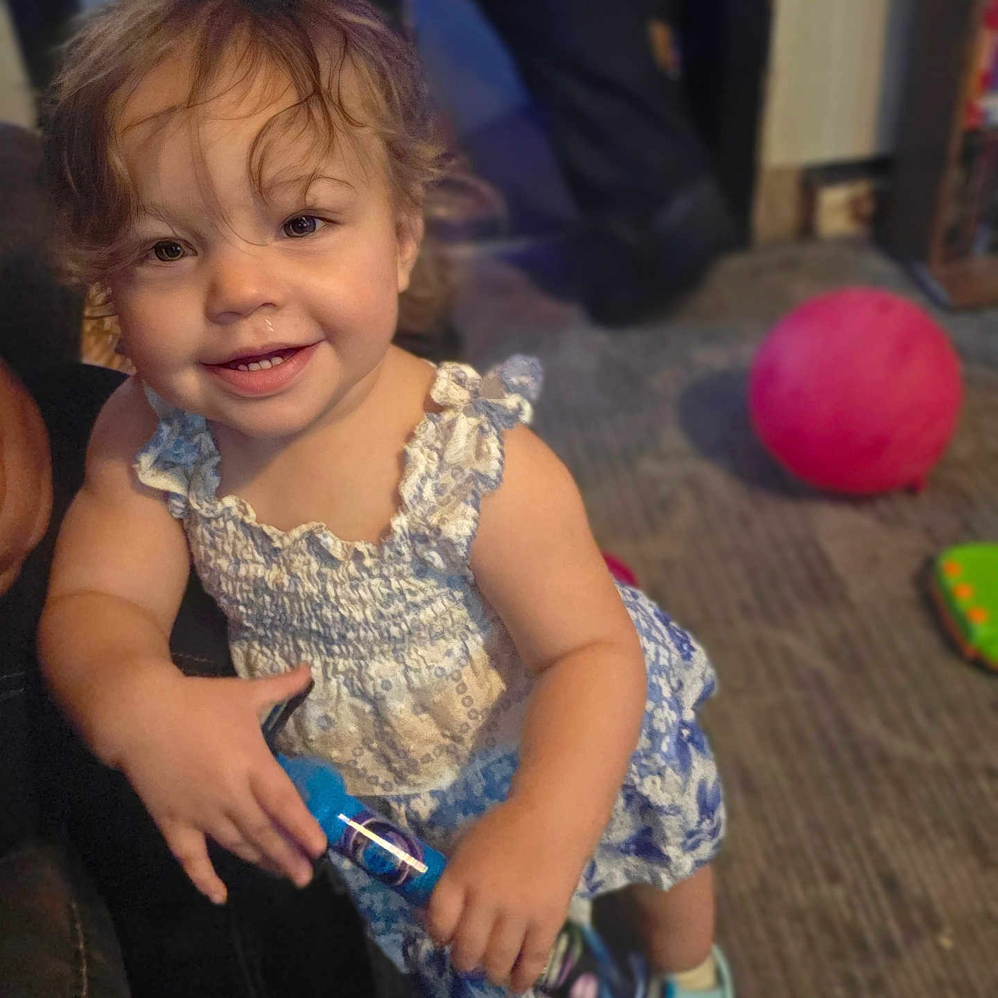 Tammy joined the competition — help win amazing prizes! toddler, child, smile, curly_hair, blue_dress, toy, indoor, carpet, footwear, happy, person, play, cute, young_child, clothing, floor, colorful, background, standing, skin