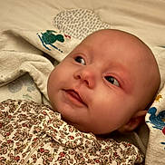 Emry is registered to the contest to win money with this photo: baby, infant, child, portrait, face, smiling, eyes, lying_down, blanket, bedding, floral_clothing, patterned_fabric, home, indoor, close_up, soft_lighting, cozy, head, newborn, photography