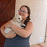 woman, puppy, dog, glasses, smile, holding, pet, outdoor, door, wall, texture, bracelet, casual_clothing, hair, happy, portrait, animal, friendship, love, cuddle