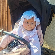 Lïna participe au concours pour gagner de l'argent avec cette photo : baby, infant, child, stroller, pram, sunhat, hat, canopy, harness, seat, bumper_bar, pink_clothing, patterned_blanket, wooden_wall, bench, outdoor, portrait, neutral_expression, sunlight, cute