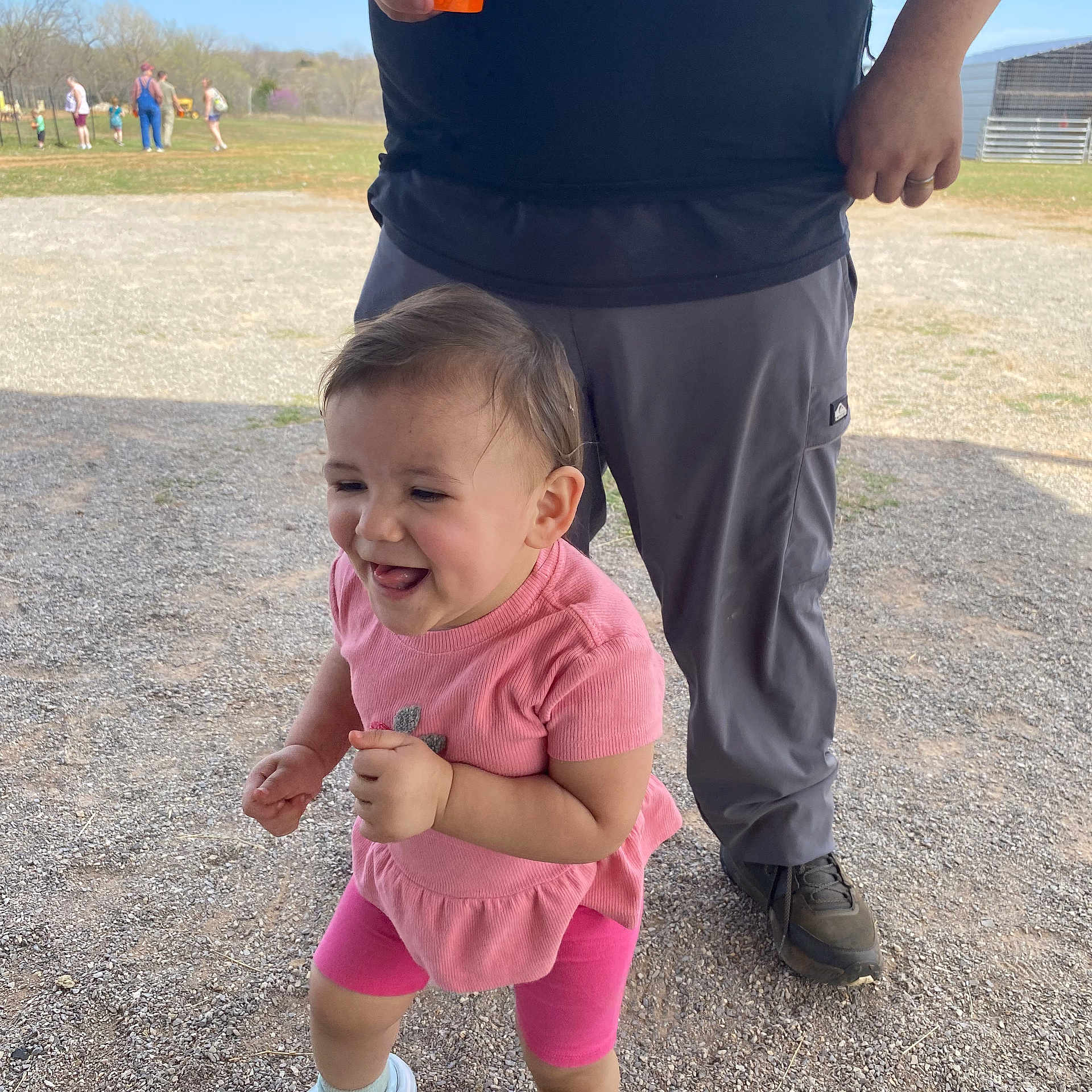 Desiree is registered to the contest to win money with this photo: toddler, child, person, outdoor, gravel, pink_clothing, shoes, smiling, happy, adult, hand, cup, sky, grass, trees, people, casual_clothing, daylight, fun, playing