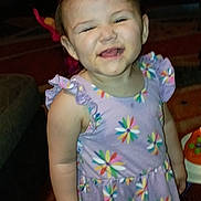 Desiree is registered to the contest to win money with this photo: toddler, child, girl, smiling, indoor, dress, floral_pattern, short_sleeves, carpet, toy, couch, happy, young_child, person, standing, cute, playful, home, colorful_clothing, baby