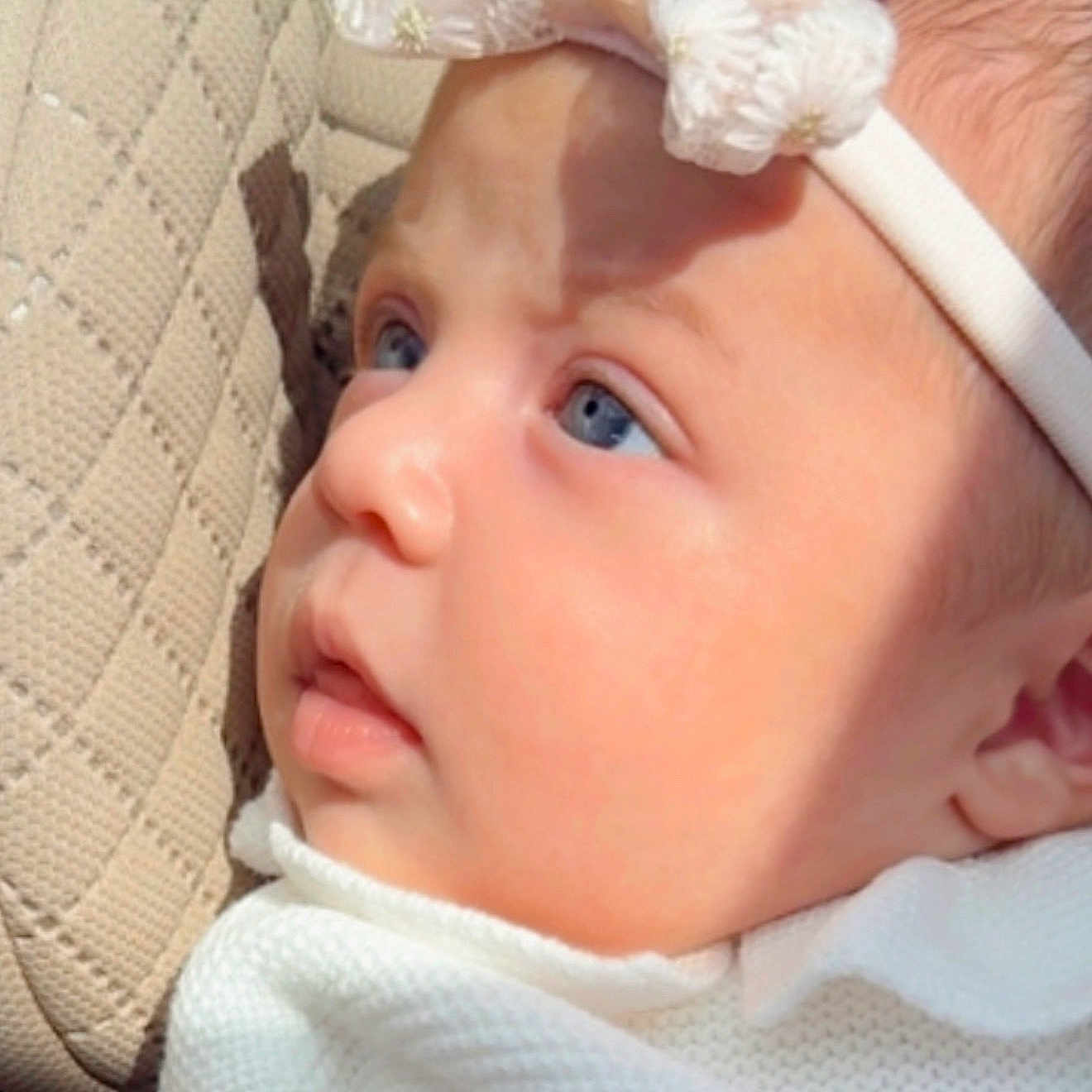 Aitana is registered to the contest to win money with this photo: baby, close_up, face, blue_eyes, headband, bow, infant, curious, skin, texture, cushion, beige, portrait, soft_light, newborn, clothing, white, side_view, child, indoors